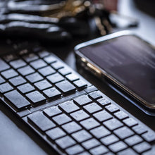 Load image into Gallery viewer, Close up to the keyboard arranged on a black table with a cellphone on a blurry background.