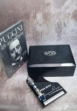 Load image into Gallery viewer, The pen arranged outside its presentation box in the piano-shaped stand with the included book.