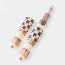 Load image into Gallery viewer, The Checkmate Fountain Pen is shown with its cap set to the side. The top of the cap and the bottom of the pen feature the cross of the King piece.