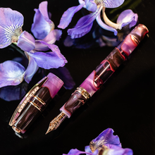 Load image into Gallery viewer, The Visconti Homosapiens Iris Garden Fountain Pen on a black background with lavender flowers.