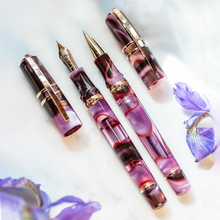 Load image into Gallery viewer, Visconti Homosapiens Iris Garden Fountain and Rollerball Pen opened on a white background with lavender flowers. It is translucent lacquer with swirls of magenta, dark red, and golden-colored trims.