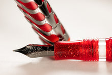 Load image into Gallery viewer, Close up to the nib and grip section of the Visconti skeleton ruby red fountain pen. The nib has an engraved decoration with the word VISCONTI on it, followed by 18KT 750, and then M for Medium point.