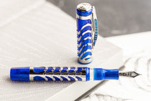 Load image into Gallery viewer, The Visconti Skeleton Sapphire Blue Fountain Pen laid horizontally with the cap placed behind it. It is a shimmering translucent blue with a silver skeleton overlay on the body and cap.