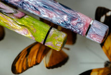 Load image into Gallery viewer, Close up to the bottom of the two Visconti Voyager Mariposa Collection pens. One is the pink and blue, the other one has green swirls in the lacquer.