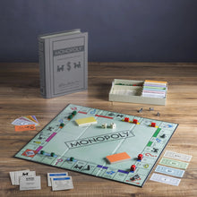 Load image into Gallery viewer, The Vintage Monopoly game board with packaging arranged on a wooden surface.
