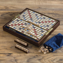 Load image into Gallery viewer, Scrabble board game set on a wooden surface with tiles and a bag.
