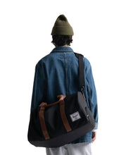 Load image into Gallery viewer, A young man facing forward and carrying the black duffle bag with the shoulder strap across his torso.
