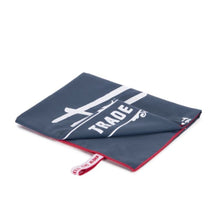 Load image into Gallery viewer, Angled view of the folded navy blue towel with red lining. A white Herschel logo is printed on it.