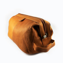 Load image into Gallery viewer, Angled view of the tan leather toiletry bag. It features a grip handle on the side.