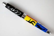 Load image into Gallery viewer, Back view of the rollerball pen, set on a white background. The Barrel of the pen has different silhouettes of Elvis on different colored backgrounds: Red, yellow, blue, and white.