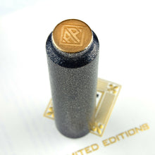 Load image into Gallery viewer, Top view of the cap set on the included envelope. It has a painting of the AP logo in lacquer and gold dust.