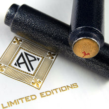 Load image into Gallery viewer, View of the bottom of the pen leaning on the barrel. The pen's bottom features the artist signature and the edition number. Both are placed on top of an envelope with the AP logo.