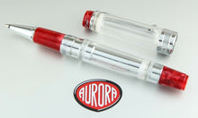 Load image into Gallery viewer, The rollerball with the cap set to the side. Both are placed on top of the included box. The pen is transparent, and has red resin accents on the grip section, the bottom of the pen, and at the top of the cap.