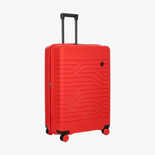 Load image into Gallery viewer, Angled front view of the 30 inch expandable red suitcase on a white background. The front features a design with wave lines, and a small black circle with the BY logo at the top right.