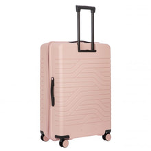 Load image into Gallery viewer, Back angled view of the hard-shell pink suitcase. It features a textured wave pattern, and a side handle for easy carrying.