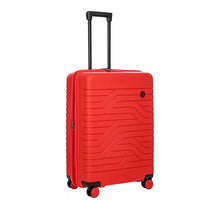 Load image into Gallery viewer, Front angled view of the red hard shell suitcase with black accents. The front panel has a design of wave lines and a small circular black logo at the top right. The telescopic handle is pulled up.