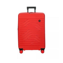 Load image into Gallery viewer, Front view of the red hard shell suitcase with black accents. The front panel has a textured wave lines design and a small circular black logo with the BY initials at the top right.