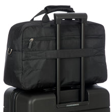 Load image into Gallery viewer, The back strap of the duffle is passed through the telescopic handle of a suitcase to keep it in place.