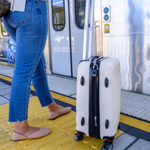 Load image into Gallery viewer, A young woman waiting to board a subway. Her suitcase zippers are secured together with a black Benji Lock.