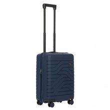 Load image into Gallery viewer, Angled front view of the navy blue hard shell suitcase with black accents. The front panel has a textured wave lines design, and a small black circular logo at the top right. The telescopic handle is fully extended.