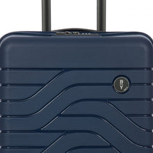 Load image into Gallery viewer, Close up to the top front of the navy blue hard shell suitcase. The wave lines design is visible with the circular black BY logo at the top right.