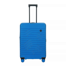 Load image into Gallery viewer, Front view of the electric blue hard shell suitcase with black accents. The panel has a textured wave lines design, and a small black circular logo with the BY initials on it.