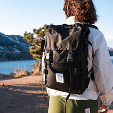Load image into Gallery viewer, A model facing forward carrying the black backpack on his shoulders.