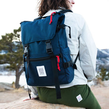 Load image into Gallery viewer, A sitting model facing into the background. They are carrying the classic navy blue backpack.