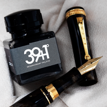Load image into Gallery viewer, Close up to the fountain pen nib resting on the cap with the ink bottle set next to them.