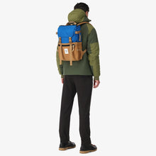 Load image into Gallery viewer, A young man wearing a green jacket carrying the blue and khaki backpack by the shoulder straps.