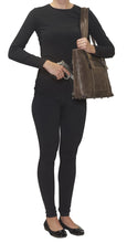 Load image into Gallery viewer, A young woman dressed in black carries the brown leather tote on her shoulder as she's pulling a gun from the compartment.