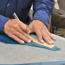 Load image into Gallery viewer, A pair of hands trimming blue leather.