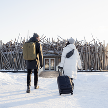 Load image into Gallery viewer, A young man and a woman carry their Thule luggage into a building on a snowy background.