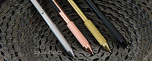 Load image into Gallery viewer, The silver, copper, brass, and black quadro pen arranged on a group of bike chains.