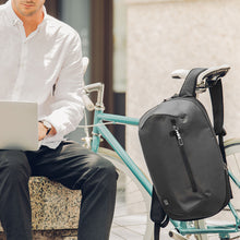 Load image into Gallery viewer, A young man sitting on a bench with a laptop. The bike next to him has the black backpack hanging from the seat.