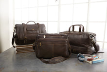 Load image into Gallery viewer, A table with three different chocolate-brown leather bags, some books, and headphones is arranged. The left one is messenger bag, the center one is a portfolio bag, and the right one is a duffle bag. It features items from the Daytrekr brand which work well as work and gym bags.