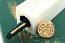 Load image into Gallery viewer, The fountain pen peeking from the rectangular presentation box. The round cap has FAO FIAT PANIS embossed in it.