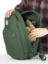 Load image into Gallery viewer, A person folding clothing into the main compartment of the green backpack.