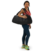 Load image into Gallery viewer, A young woman in a gym outfit carrying the black duffle bag on her shoulder.