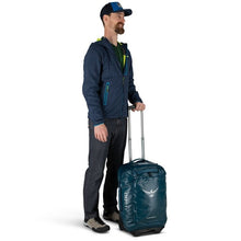 Load image into Gallery viewer, A young man holding the blue wheeled duffle by the telescopic handle.