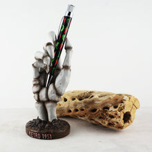 Load image into Gallery viewer, Front view of a skeleton hand holding a pen. A piece of decorative wood is placed behind it.