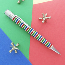 Load image into Gallery viewer, Side view of the Origin pen arranged on a red, blue and green background with metallic jax toys.