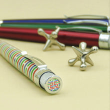 Load image into Gallery viewer, Angled top view of the Origin pen with a red, green, and blue lacquer set of pens and metallic jax toys behind it.
