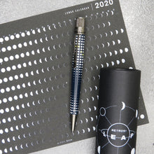 Load image into Gallery viewer, Side view of the Leap pen laying on the Lunar Calendar print next to the gift tube.