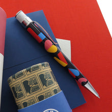 Load image into Gallery viewer, Side view of the 2021 Love Stamp Pen arranged with the gift tube, and blue and red paper prints.
