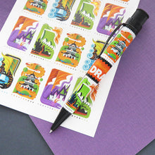 Load image into Gallery viewer, Side view of the pen laid on a card with cartoon dragons on post stamps.
