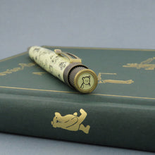 Load image into Gallery viewer, Angled top disk view of the pen on top of a green book. It features drawing of Winnie The Pooh