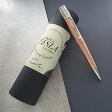Load image into Gallery viewer, The pen leaning on the gift tube on a textured gray and black paper.
