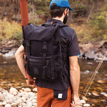 Load image into Gallery viewer, A young man hiking in the wilderness, carrying the black backpack.
