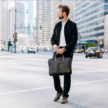 Load image into Gallery viewer, A young man carrying the briefcase by the leather handles in an urban background.